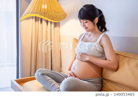 Pregnant woman sits with her hands gently stroking her belly, showing love, warmth and concern for the baby on the bed with a happy smile. Pregnant woman sits with her hands gently stroking her belly, showing love, warmth and concern for the baby on the bed with a happy smile. 140053465