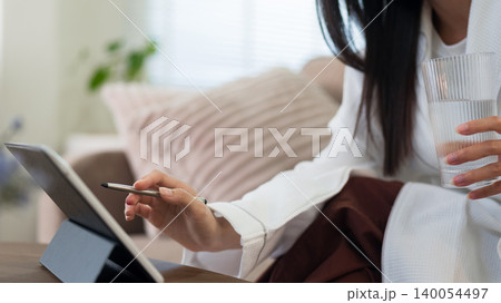 Asian women drinking water holding glass using digital tablet stylus pen writing morning routine healthy lifestyle wellness habit at home living room sofa Asian women drinking water holding glass using digital tablet stylus pen writing morning routine healthy lifestyle wellness habit at home living room sofa 140054497