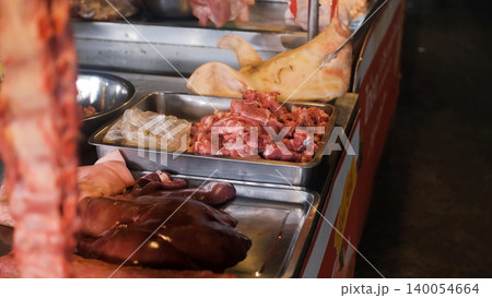 Raw meat counter displaying various meat cuts and a whole pig head at an indoor traditional Thai market. Traditional butchery concept 140054664