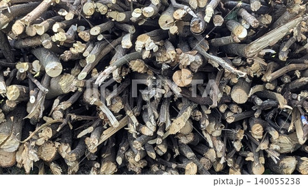 A high-angle close-up photo shows a densely packed pile of freshly cut wood branches and logs. The image is filled with the various textures and colors of the wood, from light to dark. A high-angle close-up photo shows a densely packed pile of freshly cut wood branches and logs. The image is filled with the various textures and colors of the wood, from light to dark. 140055238