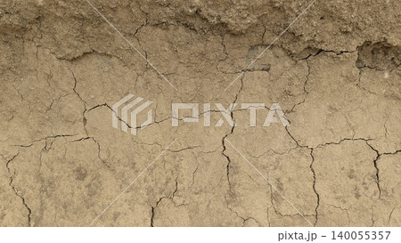 A detailed close-up of rough, textured earth showing a mix of fine dirt, gravel, rocks. The surface transitions from dark gray on the left to light brown on the right. 140055357
