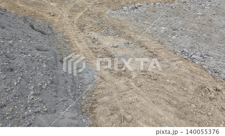 The image shows a construction site with gray gravel on the left right of a central path of light brown dirt. Tire marks are visible on the disturbed earth. 140055376