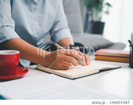 Professional writing in open notebook with red coffee cup on bright office desk, showing note taking, business planning, creative ideas, productivity, focus, and organized workspace Professional writing in open notebook with red coffee cup on bright office desk, showing note taking, business planning, creative ideas, productivity, focus, and organized workspace 140055487