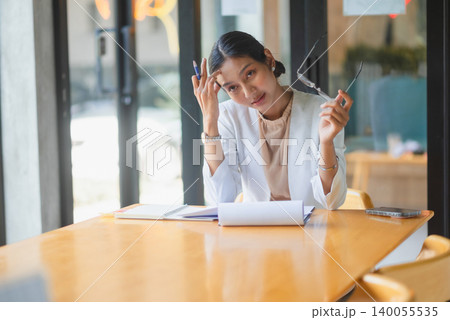 Tired businesswoman removing glasses while reviewing office documents at meeting table, showing workplace stress, business challenge, financial report problem, deadline pressure, and heavy workload. Tired businesswoman removing glasses while reviewing office documents at meeting table, showing workplace stress, business challenge, financial report problem, deadline pressure, and heavy workload. 140055535