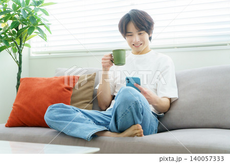 ソファで飲み物を持ってスマホを見る若い日本人男性 ソファで飲み物を持ってスマホを見る若い日本人男性 140057333