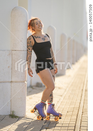 Smiling young woman with tattoos enjoying roller skating outdoors Smiling young woman with tattoos enjoying roller skating outdoors 140057509