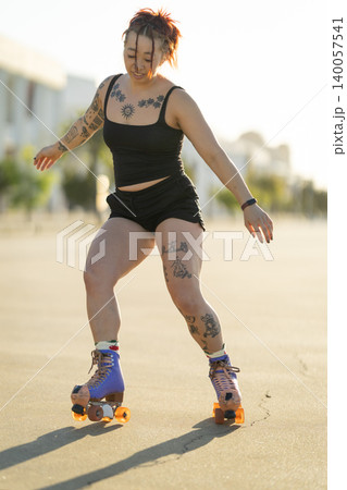 Tattooed woman happily roller skating outdoors 140057541