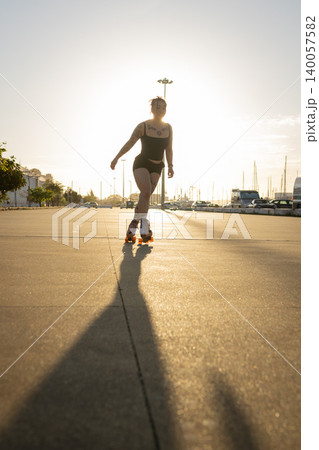 Young woman roller skating on urban street at sunset creating long shadow 140057582