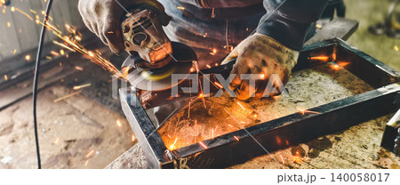 Skilled worker using an angle grinder to cut and grind metal, generating bright sparks in a workshop environment, focusing on craftsmanship and industrial work. 140058017