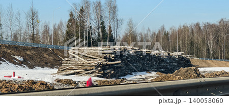 Large pile of cut birch tree logs representing deforestation and environmental impact due to expanding infrastructure, with dirt and snow on the ground beside a new road. Large pile of cut birch tree logs representing deforestation and environmental impact due to expanding infrastructure, with dirt and snow on the ground beside a new road. 140058060