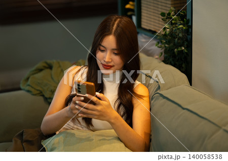 Young woman browsing on smartphone while sitting comfortably on sofa at home 140058538