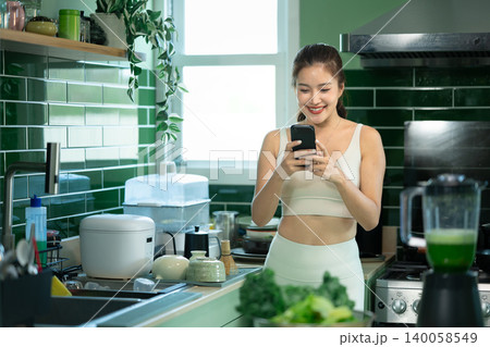 Woman checking smartphone after making green smoothie Woman checking smartphone after making green smoothie 140058549