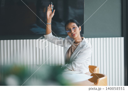 Businesswoman raising hand with pen during office meeting, showing engagement, teamwork and active participation while using tablet and notes in a collaborative corporate team discussion. Businesswoman raising hand with pen during office meeting, showing engagement, teamwork and active participation while using tablet and notes in a collaborative corporate team discussion. 140058551