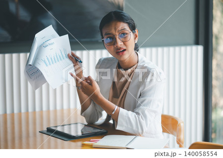 Concerned businesswoman pointing at sales report in office meeting, highlighting chart data and performance issues while using tablet and pen to explain results and financial concerns. 140058554