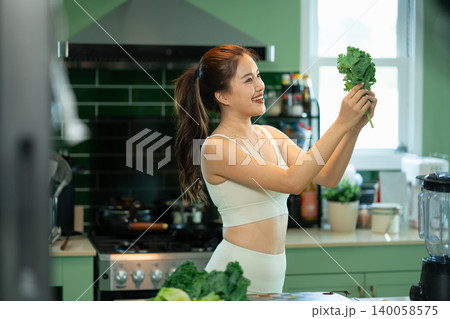 Smiling woman holding fresh kale leaves in home kitchen Smiling woman holding fresh kale leaves in home kitchen 140058575
