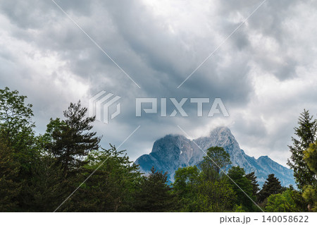 Mountain peak covered by dramatic storm clouds above dense forest landscape Mountain peak covered by dramatic storm clouds above dense forest landscape 140058622
