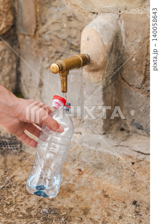 Hand filling plastic bottle with drinking water from public stone fountain 140058643