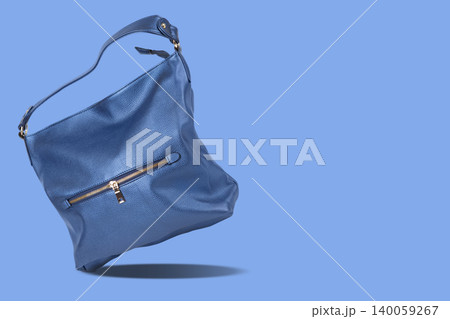Levitation of blue metallic leather handbag with gold zipper isolated on blue background. Floating female hobo bag casting a drop shadow, creative fashion concept. 140059267
