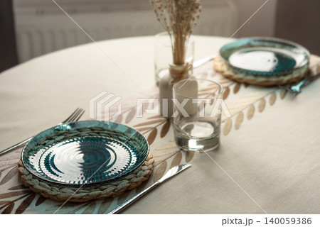 Cozy dining table setting with blue glass plates and soft sunlight Cozy dining table setting with blue glass plates and soft sunlight 140059386