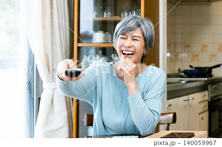 リモコンを手に楽しそうにテレビを見るシニア女性 リモコンを手に楽しそうにテレビを見るシニア女性 140059967