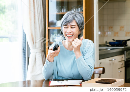 リモコンを手に楽しそうにテレビを見るシニア女性 リモコンを手に楽しそうにテレビを見るシニア女性 140059972