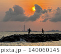 Silhouettes of fishermen on rocks at sunset with industrial background. 140060145
