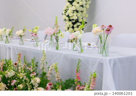 Wedding table is arranged with small vases of flowers for gathering in plain indoor space. Wedding table is arranged with small vases of flowers for gathering in plain indoor space. 140061201