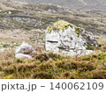 Weathered rock formations covered in green moss stand out against a hilly landscape of dry heather and grass. 140062109