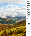 Low clouds hang over a vast valley filled with dense green forests and open fields. 140062113