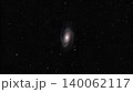 A wide-field astrophotography image showing the Bode's Galaxy, Messier 81, a spiral galaxy centered among a dense field of distant stars against black outer space. 140062117