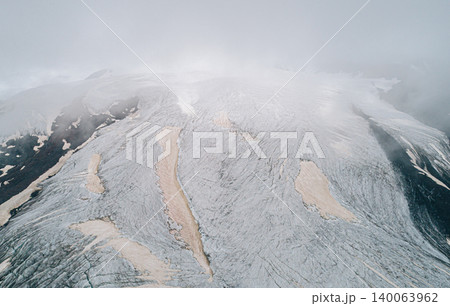 Aerial above cracked epic glacier Elbrus Caucasus mountain. Snow-capped highest peaks in fog clouds, glacier melting. 140063962