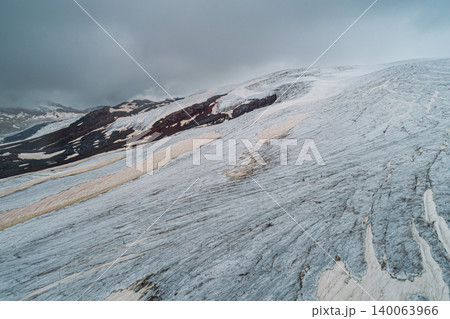 Aerial above cracked epic glacier Elbrus Caucasus mountain. Snow-capped highest peaks in fog clouds, glacier melting. 140063966