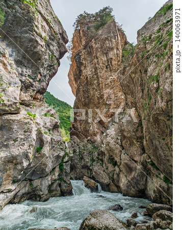 Towering rock walls surround a rushing river in a spectacular mountain gorge during daytime 140063971
