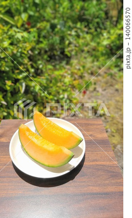 新緑が美しい屋外で撮影された白いお皿に並ぶ瑞々しい赤肉カットメロン 140066570