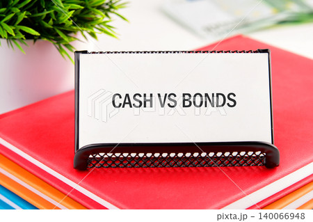 A financial concept card showing Cash vs Bonds rests on a stack of red and orange books A financial concept card showing Cash vs Bonds rests on a stack of red and orange books 140066948