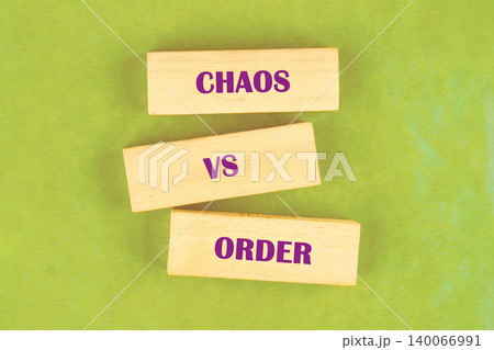 Three rectangular wooden blocks are arranged on a bright green surface, forming a conceptual stack. The words CHAOS, VS, and ORDER are printed on the blocks in purple text 140066991