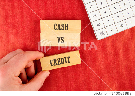 A hand positions a CREDIT wooden block near CASH and VS blocks on a textured red surface 140066995