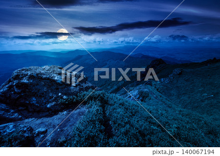 picturesque mountainous countryside scenery at night. full moon over dynamic sky above the distant valley. green meadows and rocks on the hill. mysterious nature scenery of carpathian mountains 140067194