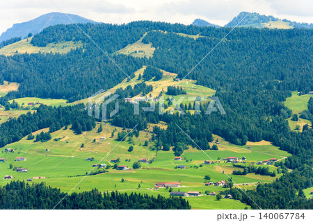 Wide landscape view of a green valley in the Swiss Alps. Rural alpine village with traditional chalets and farms on grassy hills, Switzerland. Pine forests and mountain in summer Wide landscape view of a green valley in the Swiss Alps. Rural alpine village with traditional chalets and farms on grassy hills, Switzerland. Pine forests and mountain in summer 140067784