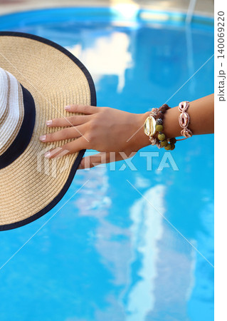 beautiful woman with nail polish touching her holiday hat by the pool. Fashion and holiday concept. beautiful woman with nail polish touching her holiday hat by the pool. Fashion and holiday concept. 140069220