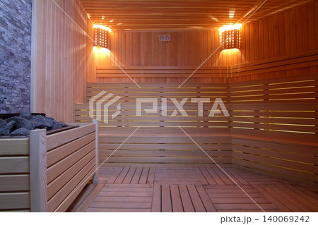 Seat in sauna room. Empty wooden steam room with stone heater.Sauna room for good health. Seat in sauna room. Empty wooden steam room with stone heater.Sauna room for good health. 140069242