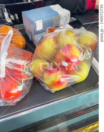 A small humble purchase of fresh apples, tomatoes, citrus fruits, and paper packs of flour on a grocery store checkout conveyor belt. A small humble purchase of fresh apples, tomatoes, citrus fruits, and paper packs of flour on a grocery store checkout conveyor belt. 140072730