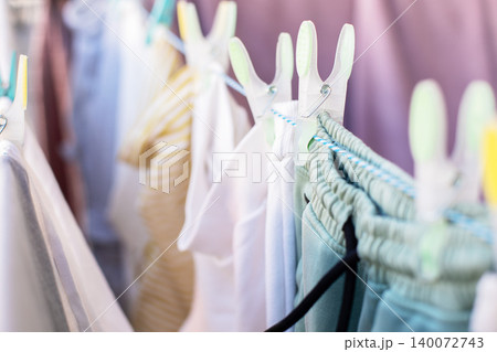 Clean colorful children and adult clothes hanging on a rope line with bright plastic clothespins on a sunny day. Clean colorful children and adult clothes hanging on a rope line with bright plastic clothespins on a sunny day. 140072743