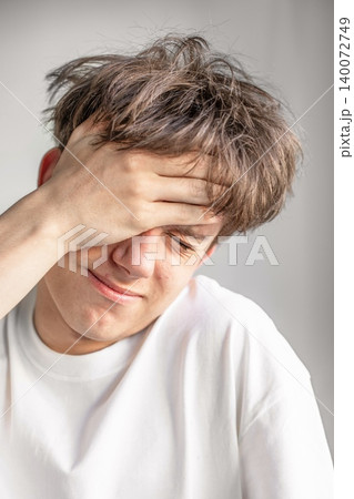 A close up of a distressed male teenager closing his eyes and pressing his hand to his forehead while experiencing severe pain, stress, or migraine A close up of a distressed male teenager closing his eyes and pressing his hand to his forehead while experiencing severe pain, stress, or migraine 140072749