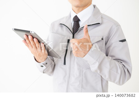 タブレットを持って親指を立てるグレーの作業着姿のミドル男性ビジネスマン白バック 140073682