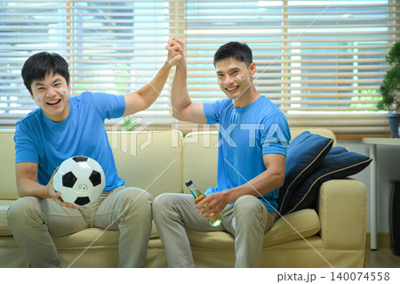 Friends celebrating soccer win at home, mens cheer on sofa after goal 140074558
