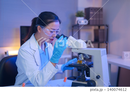 Female scientist using a microscope to analyze samples Female scientist using a microscope to analyze samples 140074612
