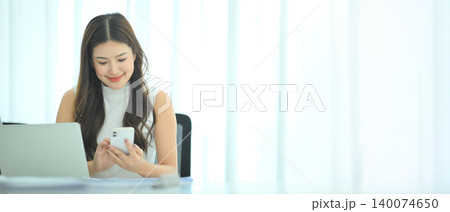 Businesswoman checking smartphone at desk in bright office 140074650