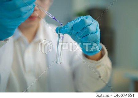 Scientist adds a purple solution into a test tube with a pipette, highlighting precision and control in laboratory chemical testing. Scientist adds a purple solution into a test tube with a pipette, highlighting precision and control in laboratory chemical testing. 140074651