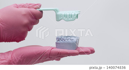 Dentist hands in pink gloves holding a purple plaster cast of teeth and lifting an empty impression tray. Copy space. Dentist hands in pink gloves holding a purple plaster cast of teeth and lifting an empty impression tray. Copy space. 140074836